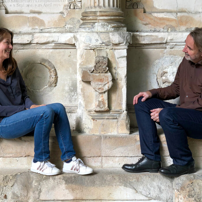 Karolin und Daniel Bräg sitzen vor einer Steinwand mit vielen Intarsien
