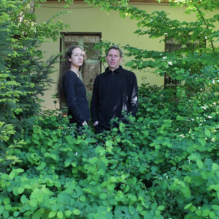 Evelyn Weinzierl & Johannes Lauter stehen vor einem Haus inmitten üppigen Grüns