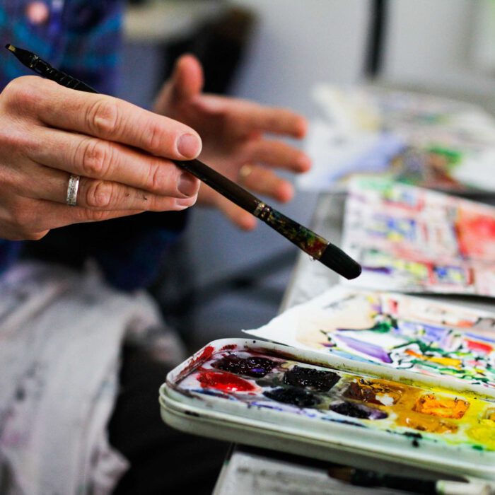 Eine Hand hält einen Pinsel und malt mit bunter Farbe