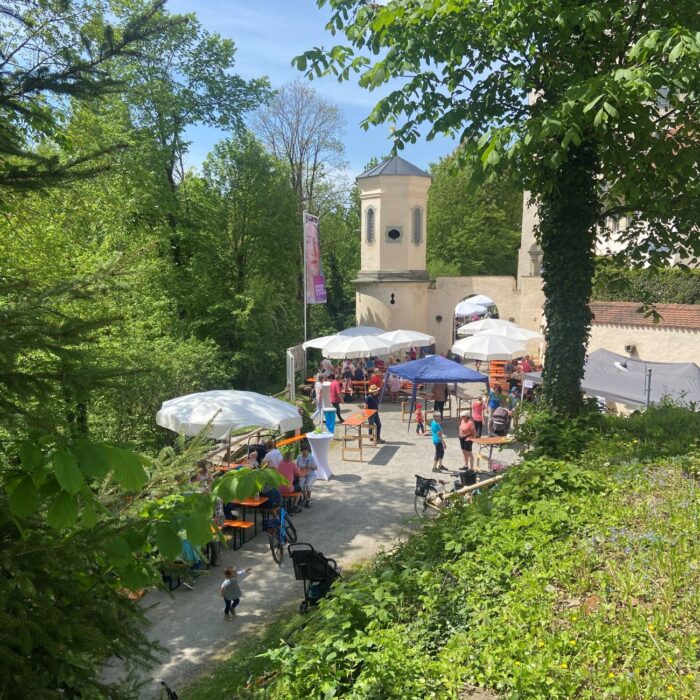 Weiße Sonnenschirme und Menschen vor dem Schloss Achberg an einem sonnigen Maitag.