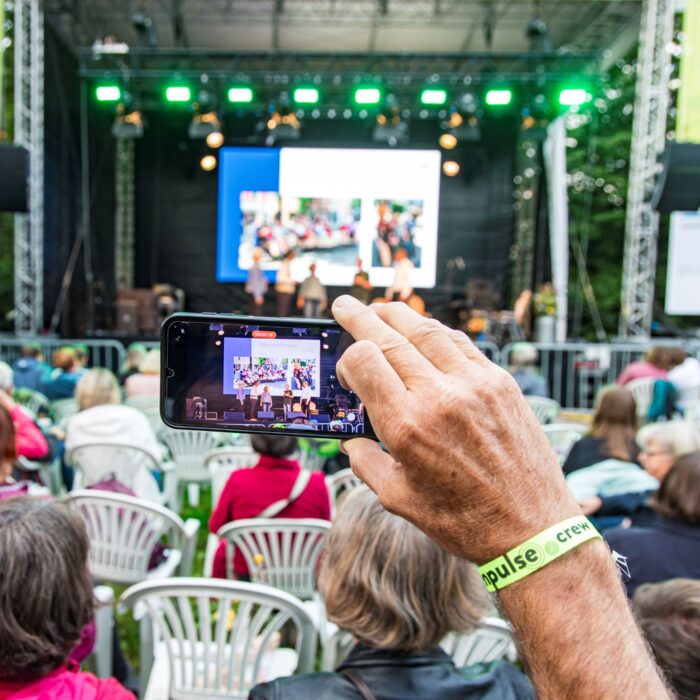 Ein Zuschauer film mit dem Handy einen Vortrag auf der großen Bühne beim GreenPulse Festival.