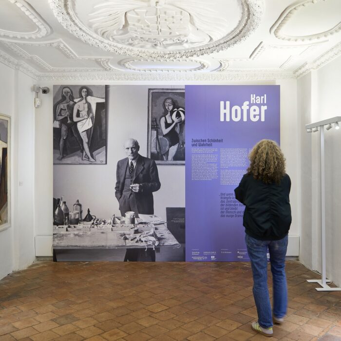 Eine Frau betrachtet die Auftaktwand der Ausstellung "Karl Hofer" auf Schloss Achberg